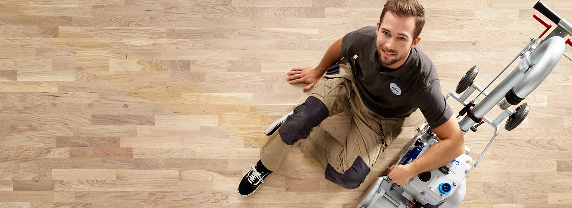Professional sitting beside a drum sander after wood floor sanding a light European oak strip floor, smiling at the camera.