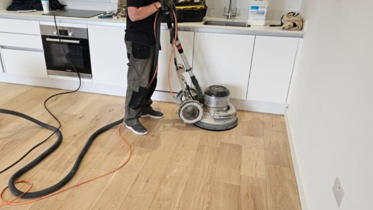 Wood floor sanding in a modern kitchen, showing a professional using a rotary buffer on an engineered oak plank floor.
