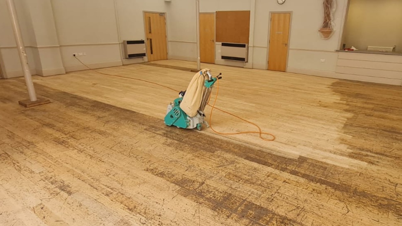 Wood Floor Sanding in New Southgate – Solid Hardwood Strip Floor Restoration Wood Floor Sanding in New Southgate on a solid hardwood strip floor mid-restoration, with a professional sander revealing a clean, lighter section.
