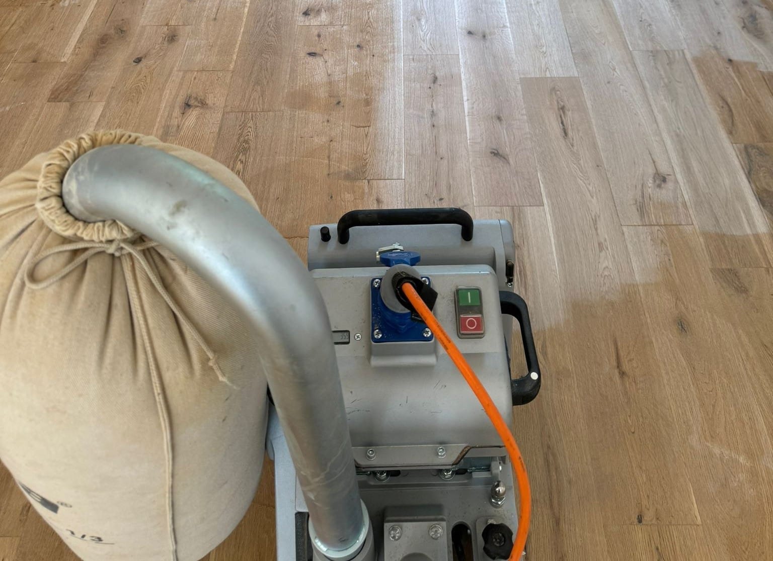 Wood Floor Sanding in New Southgate on a solid oak plank floor, shown close-up with a professional drum sander and dust bag mid-pass.