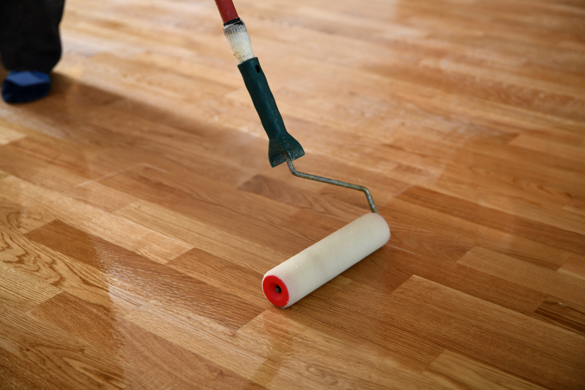 Wood Floor Sanding in New Southgate with lacquer being rolled onto a freshly sanded oak hardwood strip floor, giving it a rich protective finish.