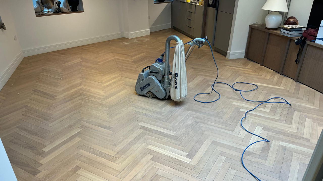 Wood Floor Sanding in New Southgate on an oak herringbone parquet floor, with a Bona belt sander positioned in the centre of a modern living space.