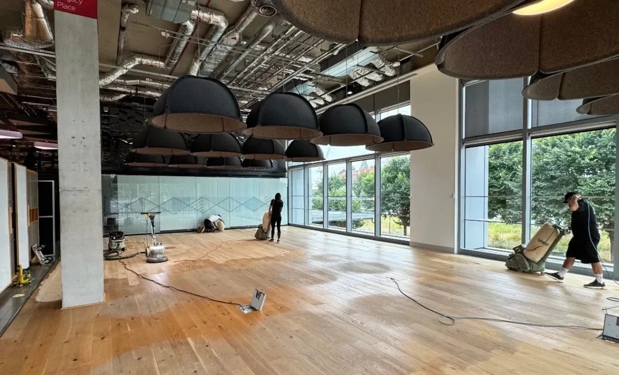 Commercial Floor Sanding in New Southgate on an engineered oak office floor, technicians sanding and restoring the surface in a modern glass-fronted workspace.