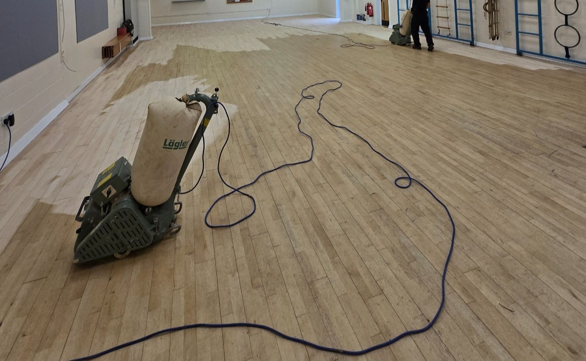 Commercial Floor Sanding in New Southgate on a sprung maple strip sports hall floor, with professional belt sanders restoring the worn surface.